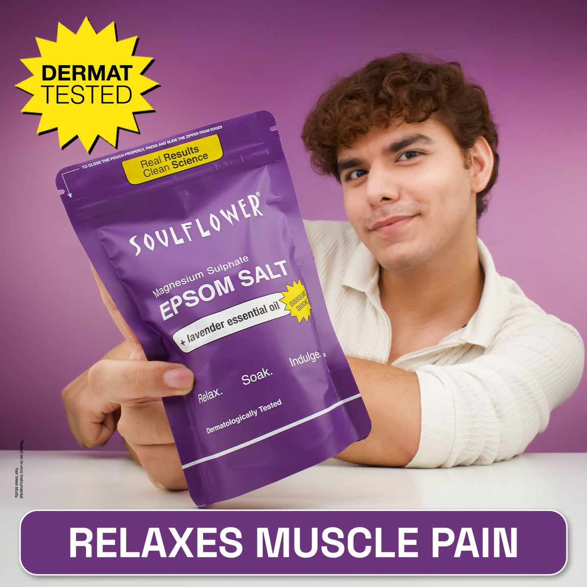 A man holding a purple stand-up pouch of Soulflower Epsom Salt against a purple background, with a yellow 'DERMAT TESTED' badge and a purple banner reading 'RELAXES MUSCLE PAIN'.